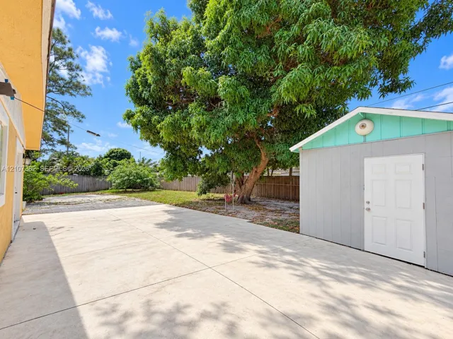 Spacious concrete patio featuring a detached storage structure and a mature canopy tree within a fenced backyard