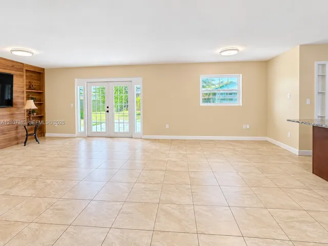 Tile flooring, wood-finish wall accent with integrated shelving, double French doors, and recessed ceiling lighting