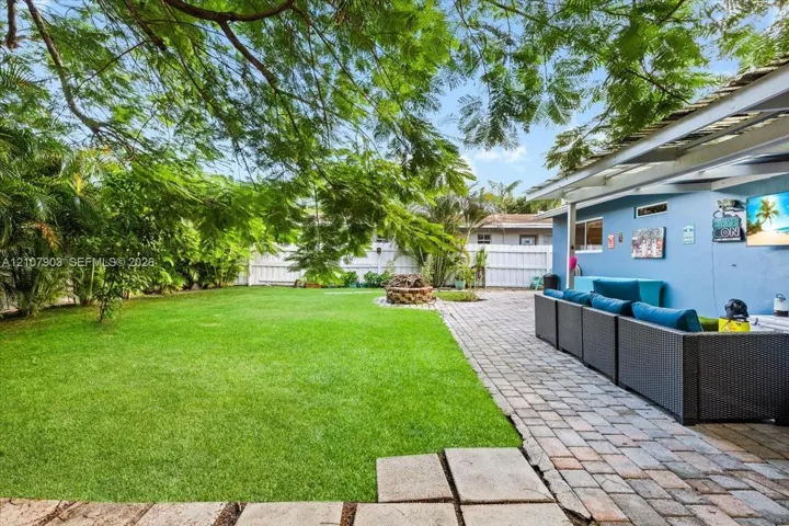 Expansive backyard featuring a manicured lawn, stone paver patio, circular stone fire pit, and mature perimeter trees