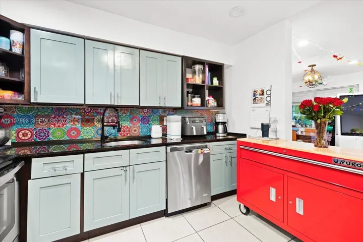 Kitchen featuring light-toned cabinetry, patterned mosaic tile backsplash, dark solid-surface countertops, stainless steel dishwasher, and recessed lighting