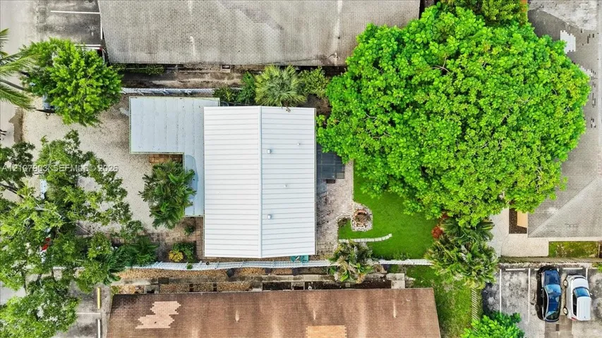 Aerial perspective featuring a metal roof structure, manicured lawn, established canopy trees, and paved parking area