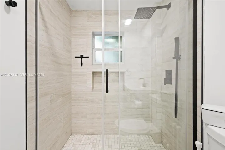Walk-in shower featuring floor-to-ceiling stone-finish tile, glass enclosure, recessed storage niche, overhead rainfall showerhead, and a mosaic tile floor