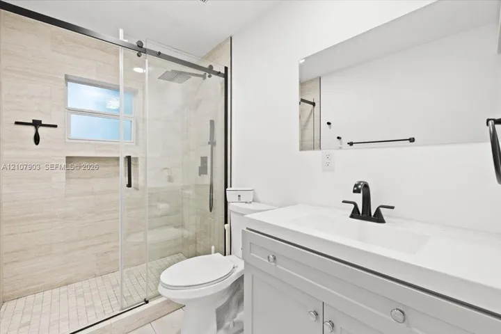 Bathroom featuring a glass-enclosed walk-in shower with horizontal stone-style wall tile and built-in recessed shelving, a vanity with a rectangular integrated sink, matte black hardware, and a frameless wall-mounted mirror
