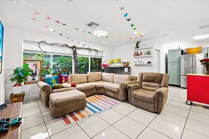 Large-format tile flooring, expansive window system, built-in wall shelving, and tall shaker-style cabinetry with stainless steel refrigerator