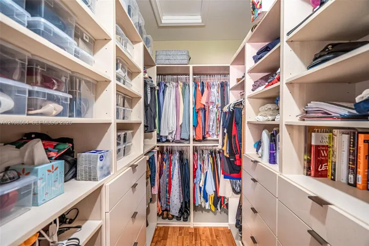 Walk-in closet featuring extensive built-in shelving, integrated hanging rods, multiple storage drawers, and wood-finish flooring