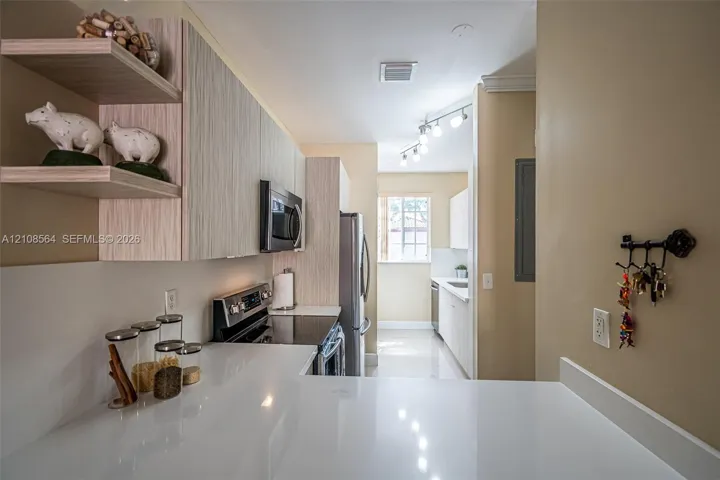 Kitchen featuring light-toned wood-finish cabinetry, quartz countertops, stainless steel appliances, open shelving, and track lighting