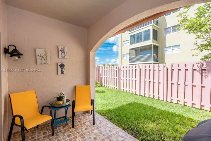Covered patio featuring an arched entryway, tile flooring, and wall-mounted exterior lighting, opening to a private lawn enclosed by a fence