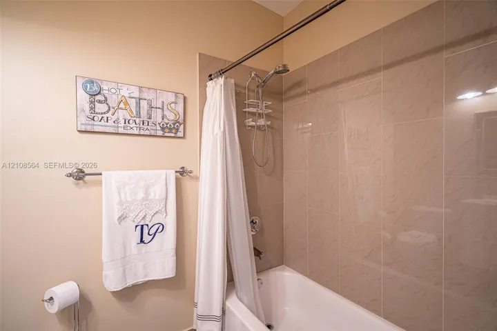 Bathtub with ceramic tile surround, integrated shower fixture, and polished metal towel bar