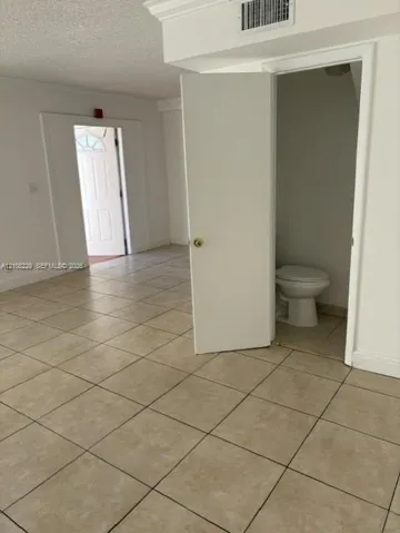 Neutral tile flooring throughout an interior space featuring a solid-core entry door with window pane detailing and a private water closet with a standard porcelain commode