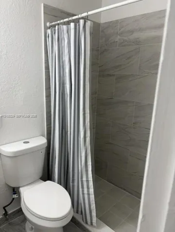 Shower enclosure featuring floor-to-ceiling large-format neutral-toned tile work and a white porcelain commode