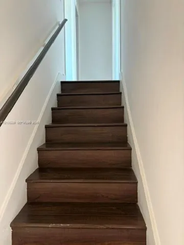 Staircase featuring wood-finish treads and a dark-toned handrail