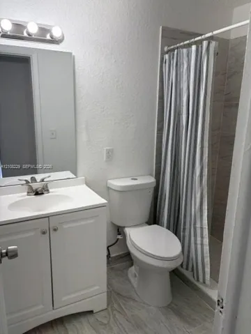 White vanity cabinet with an integrated basin, three-light wall-mounted fixture, polished chrome faucet, and neutral-toned tiled flooring