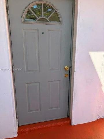 Gray four-panel door featuring a semi-circular transom window, brass-finish hardware, and a door viewer