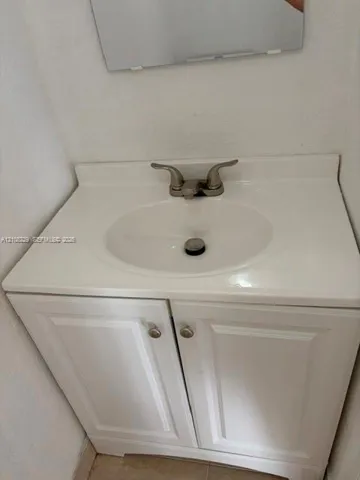 White vanity cabinet with recessed panel doors, integrated sink countertop, and dual-handle metal faucet