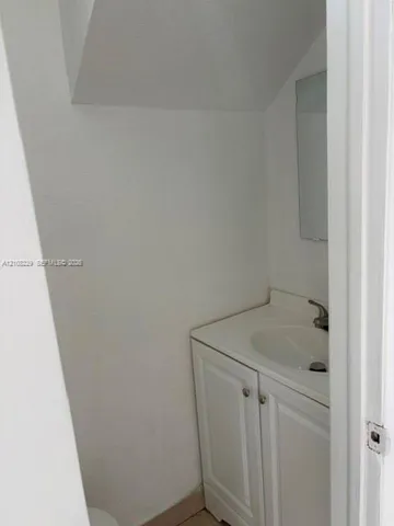 Vanity cabinet with white raised-panel doors, integrated sink countertop, single-handle faucet, and wall-mounted mirror