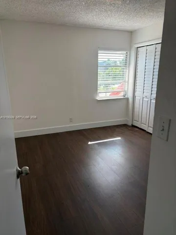 Room featuring wood-finish flooring, white walls, and a window with horizontal blinds, complemented by white bi-fold closet doors
