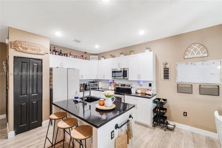 Kitchen featuring white shaker-style cabinetry, an island with a stone-surface countertop, wood-finish flooring, recessed lighting, and an integrated microwave
