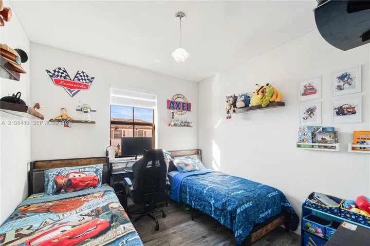 Room featuring wood-finish flooring, a central pendant light fixture, and a window with a retractable shade