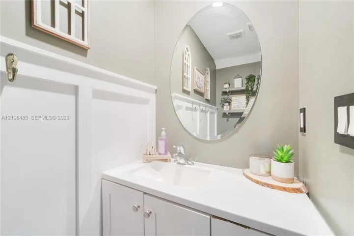 Oval wall-mounted mirror, white vanity cabinet with a integrated sink, polished chrome faucet, and board-and-batten wall detailing