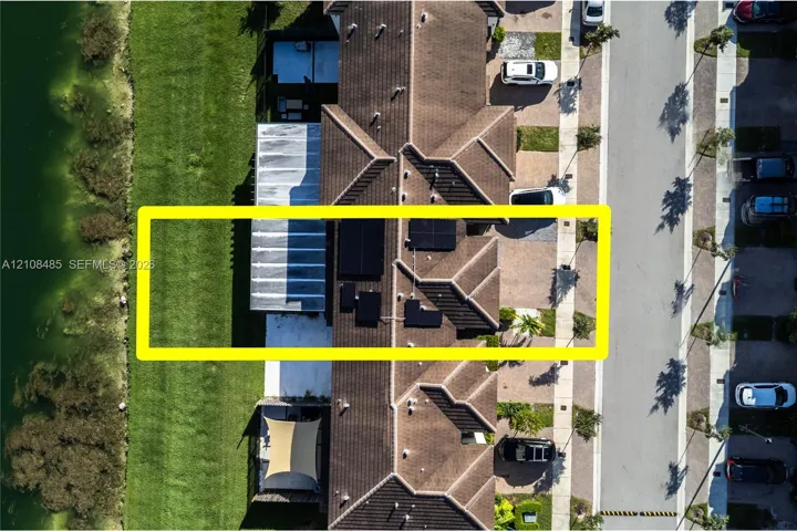 Aerial view featuring a tile roof, roof-mounted solar panels, paved driveway, and waterfront positioning