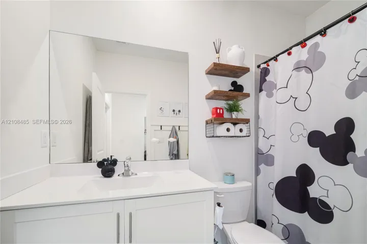 White vanity with a rectangular undermount sink, countertop, and a large frameless wall-mounted mirror