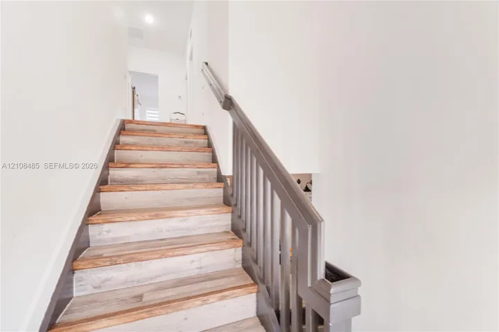 Staircase featuring wood-finish treads and a painted railing with vertical balusters