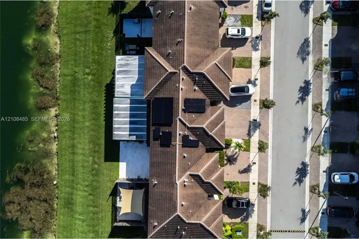 Aerial perspective of a multi-unit property featuring tiled roof lines, integrated solar energy panels, concrete hardscaping, and a grassed area bordering a water feature