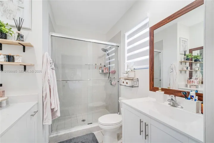 Bathroom featuring a vanity with a white countertop and rectangular undermount sink, a large wood-framed mirror, walk-in shower with glass enclosure, and wall-mounted shelving
