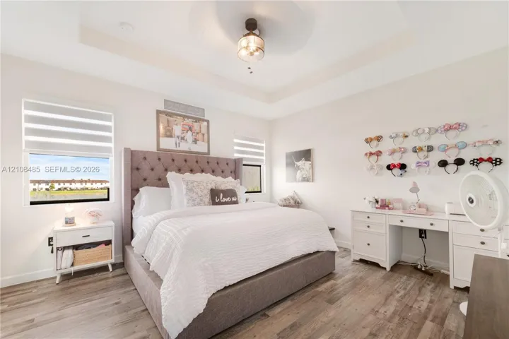 Tray ceiling with center-mounted light fixture, wood-finish flooring, and dual-layered window shades