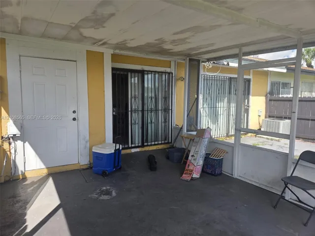 Enclosed patio featuring a concrete floor, metal screening, a solid core entry door, and metal security bars on sliding glass doors