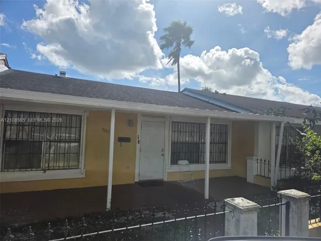 Single-story residence featuring a covered front porch, exterior metal window security bars, a concrete front patio, and a perimeter metal fence with masonry pillars