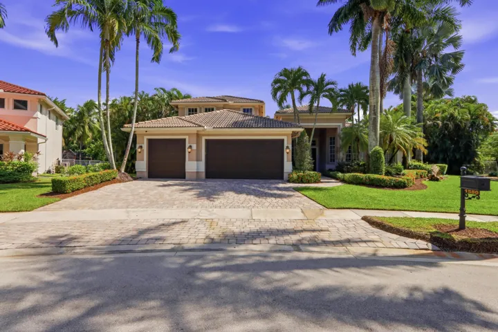 Multi-hipped tile roof, a three-car garage, and a paved stone driveway surrounded by manicured landscaping and mature palm trees