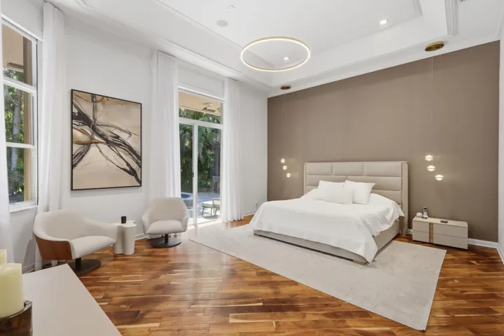 Tray ceiling with recessed lighting, wood-finish flooring, circular pendant chandelier, accent wall, and floor-to-ceiling glass patio doors