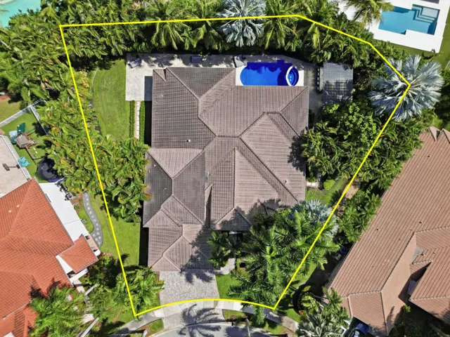 Aerial view of property featuring a hip roof, swimming pool with integrated spa, stone-paver driveway, and manicured landscaping