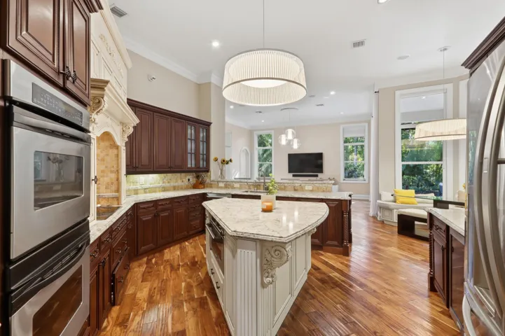 Kitchen featuring wood-finish flooring, stone countertops, custom cabinetry, stainless steel double wall ovens, and an expansive center island