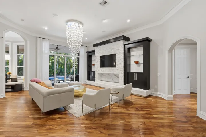 Formal living space featuring wood-finish flooring, a floor-to-ceiling stone-textured fireplace with built-in dark wood cabinetry, an intricate crystal chandelier, and arched entryways