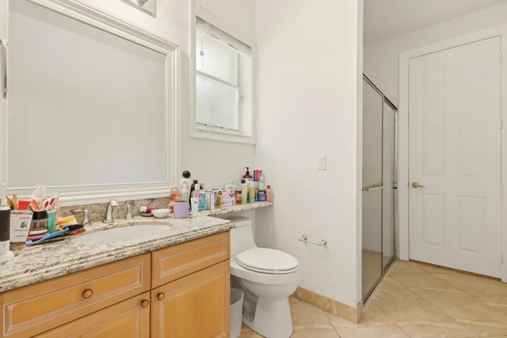 Bathroom featuring a wood-finish vanity with a stone-composite countertop, integrated sink, large framed mirror, and tiled flooring