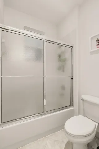Shower enclosure with chrome-finished sliding glass doors, and a standard-height porcelain toilet