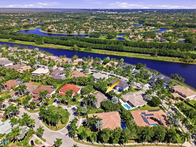 Aerial perspective of a residential property situated in a suburban community featuring canal-side positioning, mature palm trees, and terracotta-style roof tiles