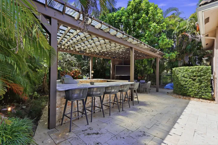 Outdoor kitchen area featuring a stone-clad bar, integrated grill, stone-tile patio, and a pergola with a slatted roof structure
