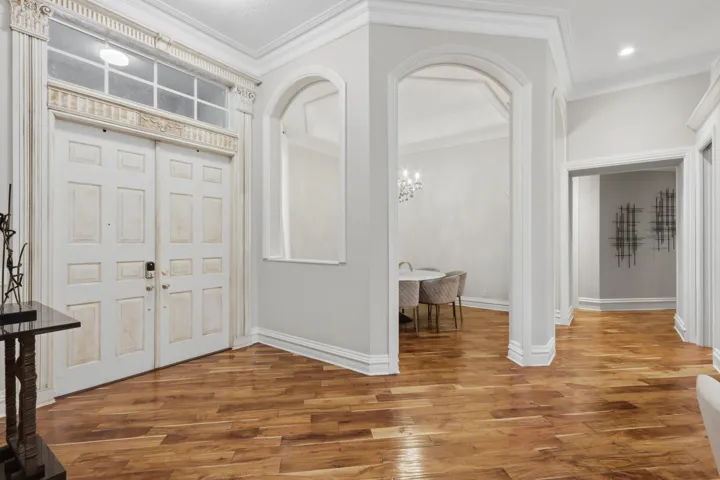 Foyer featuring wood-finish flooring, double entry doors with transom window, arched architectural openings, and extensive crown molding