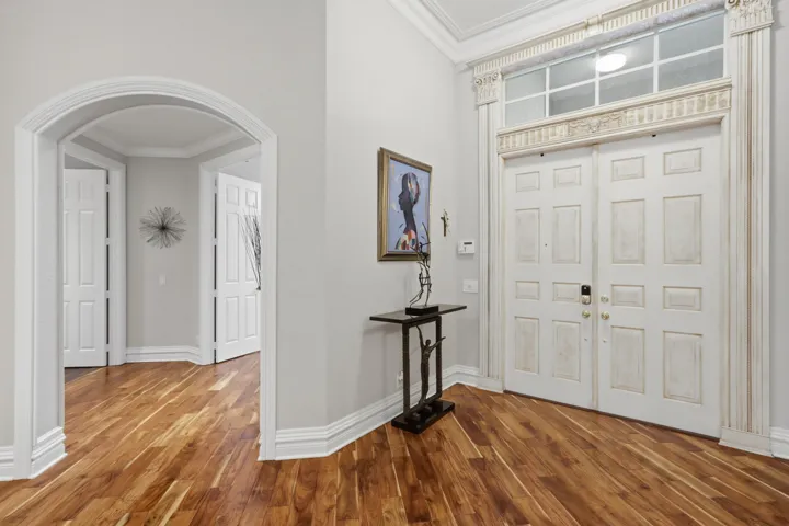 Entryway featuring dual paneled doors with decorative transom window, architectural crown molding, arched entryways, and wood-finish flooring