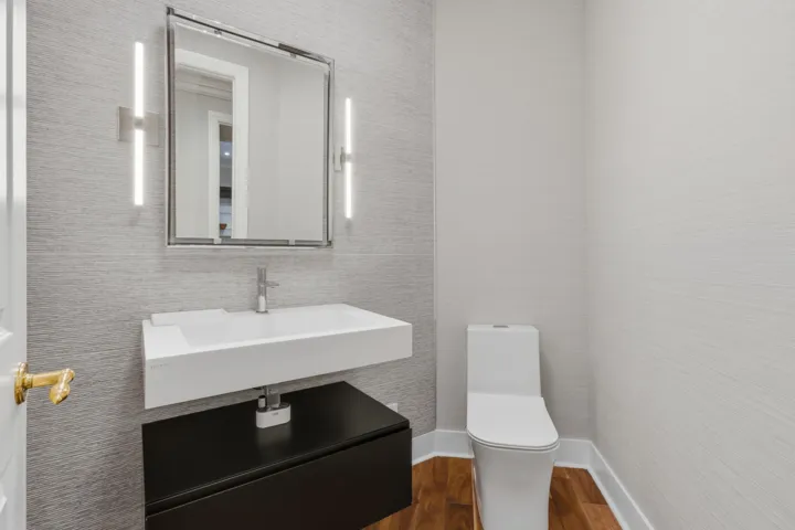 Wall-mounted vanity with a rectangular sink, dual vertical LED sconces, textured wall covering, and wood-finish flooring