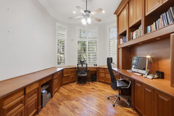 Custom built-in wood cabinetry, integrated desk workspace, bay windows with plantation shutters, wood-finish flooring, and crown molding