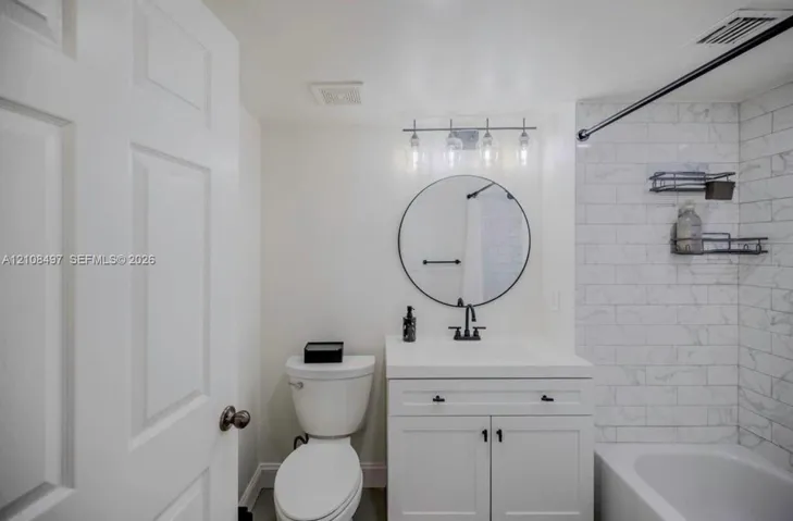 Bathroom featuring a vanity with integrated sink, circular wall-mounted mirror, matte black hardware, and tub surround with subway tile finish