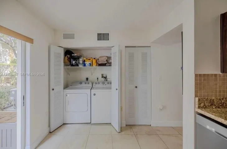 Laundry closet featuring side-by-side appliances, overhead shelving, and louvered folding doors, complemented by tile flooring and an additional louvered-door closet