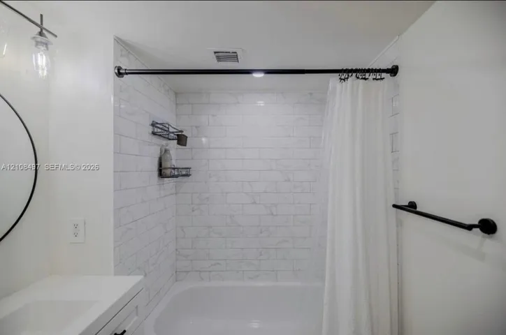 Full bathroom featuring a tub-shower combination with white subway-style tiling, a vanity with a white countertop, a circular wall-mounted mirror, and matte black fixtures