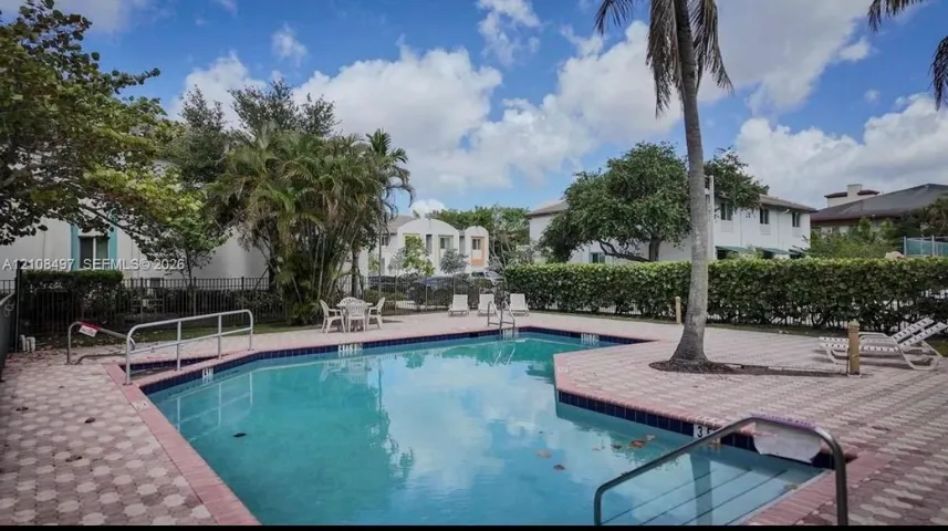 Swimming pool with a paved deck, perimeter hedging, and metal fencing