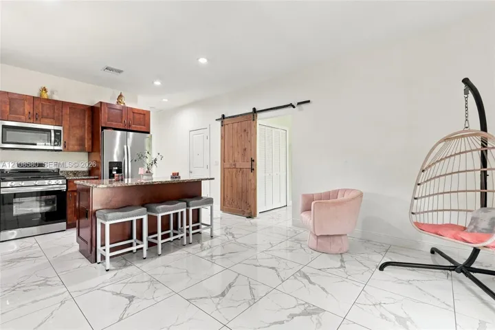 Kitchen featuring wood cabinetry, stone-finish countertops, stainless steel appliances, polished stone-finish flooring, and a sliding barn door