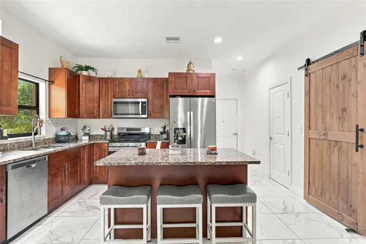 Kitchen featuring wood cabinetry, stone-surface countertops, stainless steel appliances, a central island, and wood-finish sliding barn door